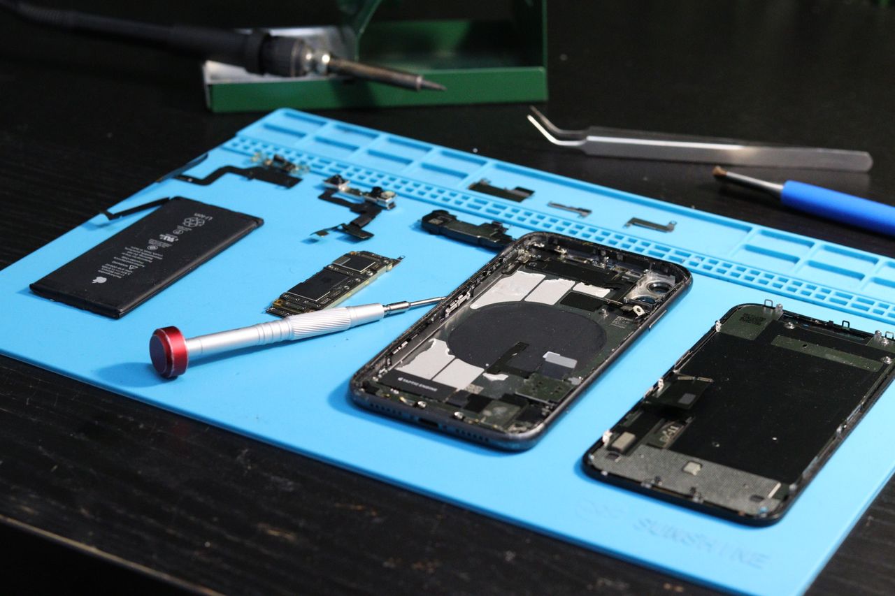 why-choose-us-01 Close-up of disassembled smartphone parts on a blue repair mat with tools.